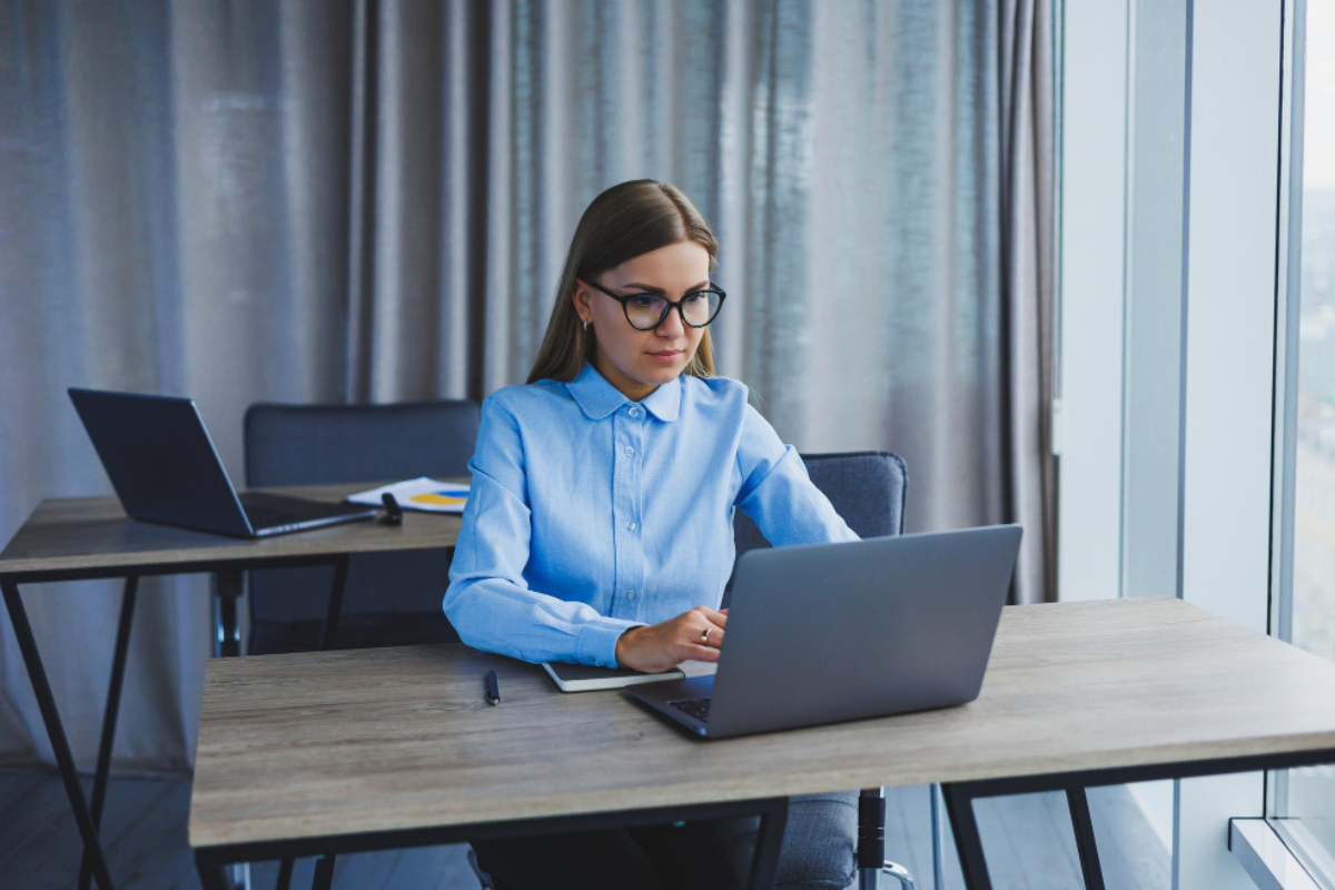 Mulher sentada usando notebook sobre uma mesa em ambiente de home office representando: XML na Reforma Tributária: o que muda?