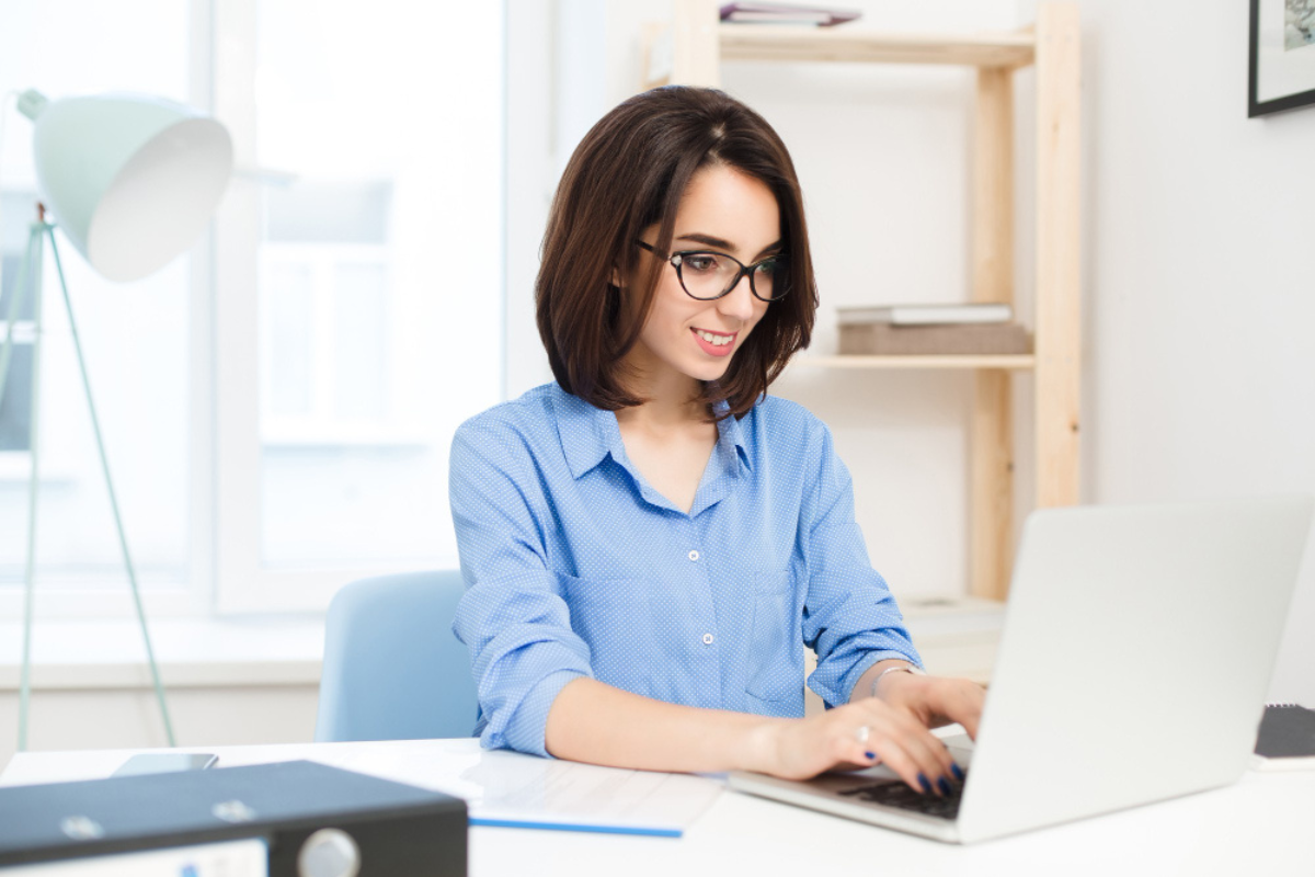 Mulher sentada trabalhando em um notebook sobre uma mesa em ambiente de escritório representando: Tabela CST: o que é e códigos.