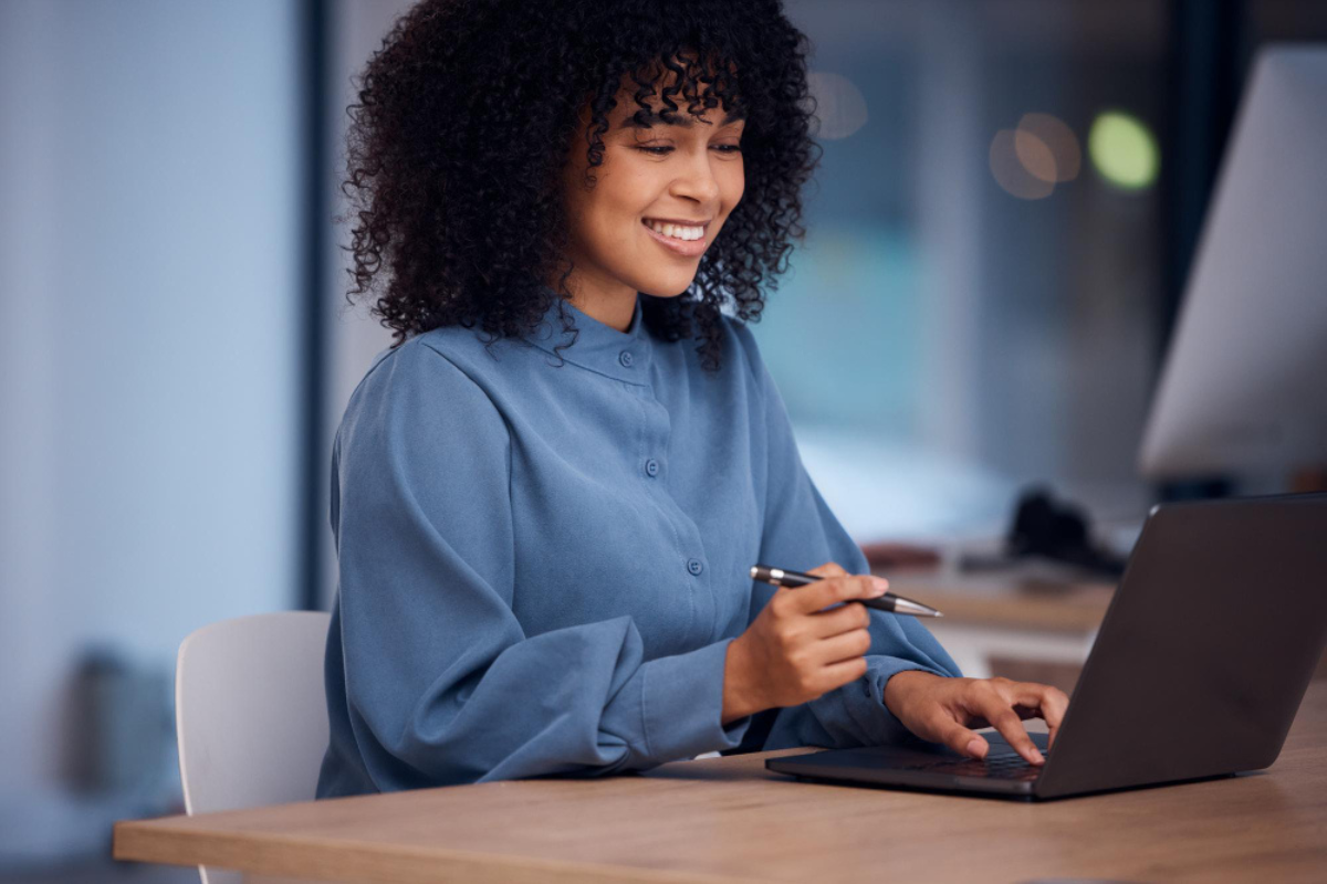 Mulher trabalhando em um notebook sobre uma mesa em ambiente de escritório representando: Emissão de nota fiscal para clientes estrangeiros na Reforma Tributária: o que muda e como preencher corretamente.