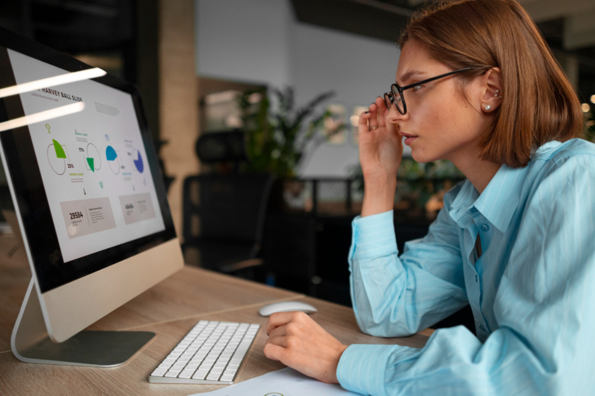 Mulher trabalhando em um computador sobre uma mesa em ambiente de escritório representando: Indicadores de desempenho que toda microempresa deveria acompanhar.