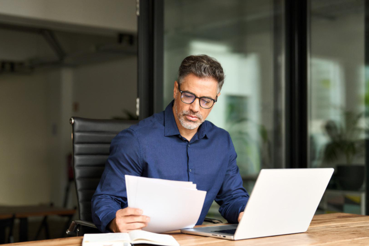 Funcionário sentado analisando documentos e relatórios sobre sua mesa de trabalho e usando notebook representando: CFOP incorreto pode gerar autuação automática na Reforma Tributária?