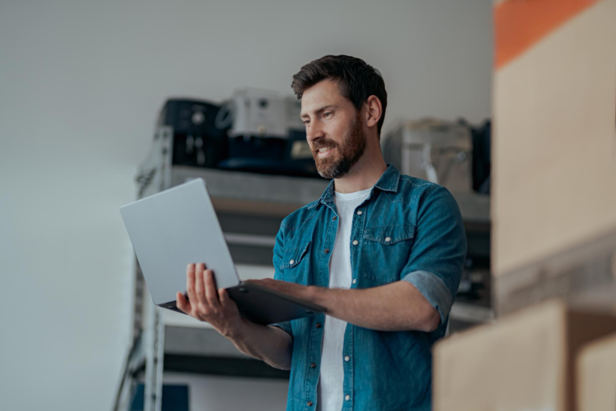 Homem de pé com notebook em uso nas mãos em ambiente de escritório representando: Como escolher fornecedores considerando crédito tributário.