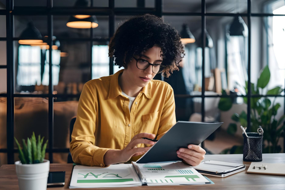 Funcionária em ambiente de escritório sentada analisando documentos, relatórios e gráficos sobre a mesa de trabalho representando: Recuperação de crédito tributário: como criar uma rotina?