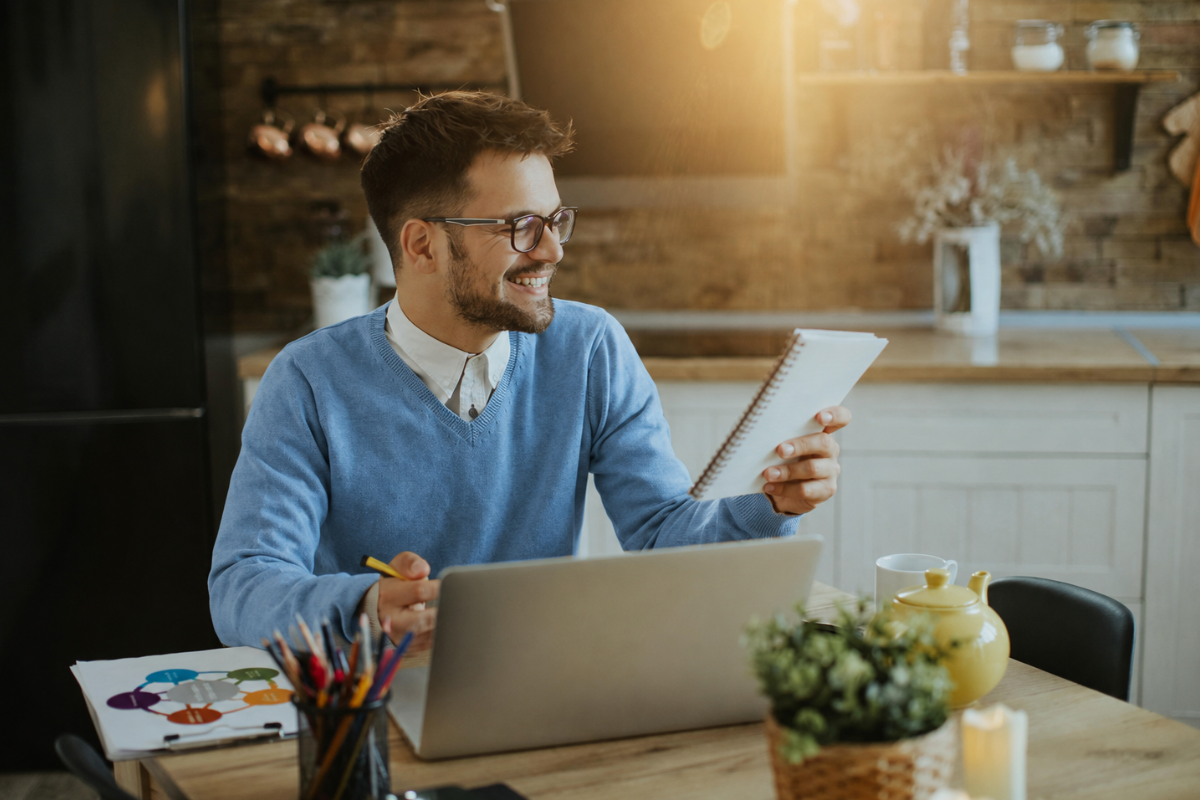 Homem trabalhando em um notebook sobre uma mesa de escritório e lendo documentos em mãos representando: Mistura de contas pessoais e empresariais: riscos legais.