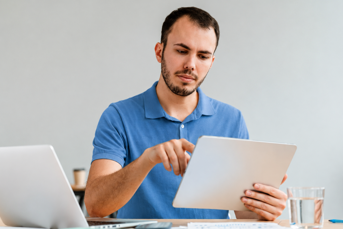 Homem em ambiente de escritório sentado lendo documentos ao lado de um notebook sobre Como preparar SPED para o novo modelo tributário.