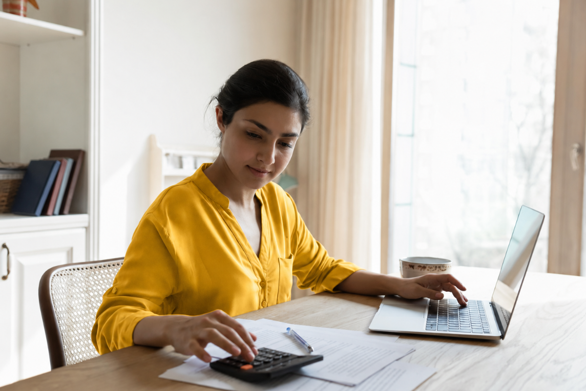 Mulher profissional de contabilidade trabalhando em um notebook sobre um mesa e usando uma calculadora em ambiente de escritório representando: Como calcular IBS e CBS na microempresa: guia de apuração passo a passo para 2026.