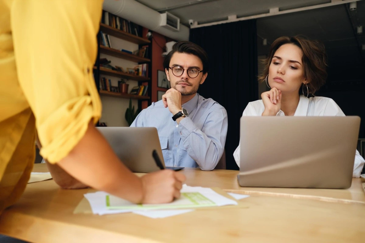 Dois empresário e uma empresária reunidos em volta de um mesa usando notebooks, analisando e fazendo anotações em documentos sobre qual o impacto do cadastro de produtos na tributação da microempresa.