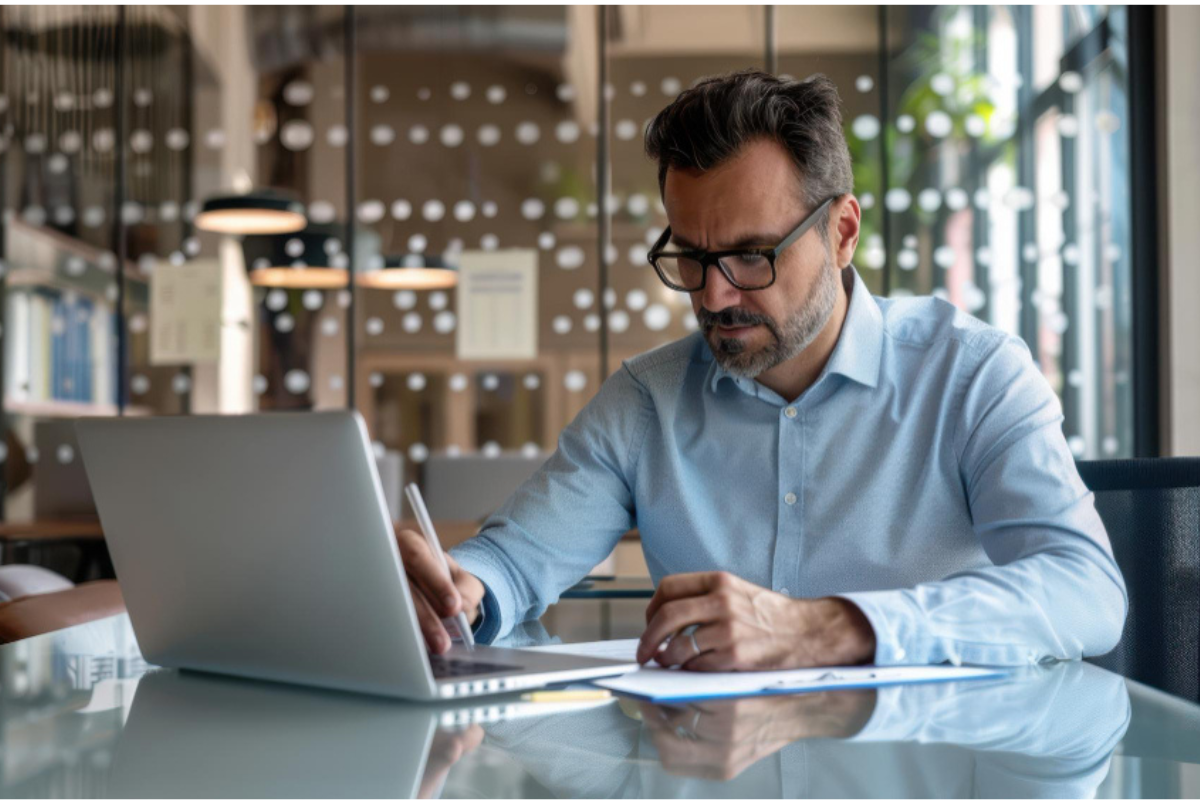 homem de azul analisando dados em seu notebook, representando: Responsabilidade tributária solidária em NF-e